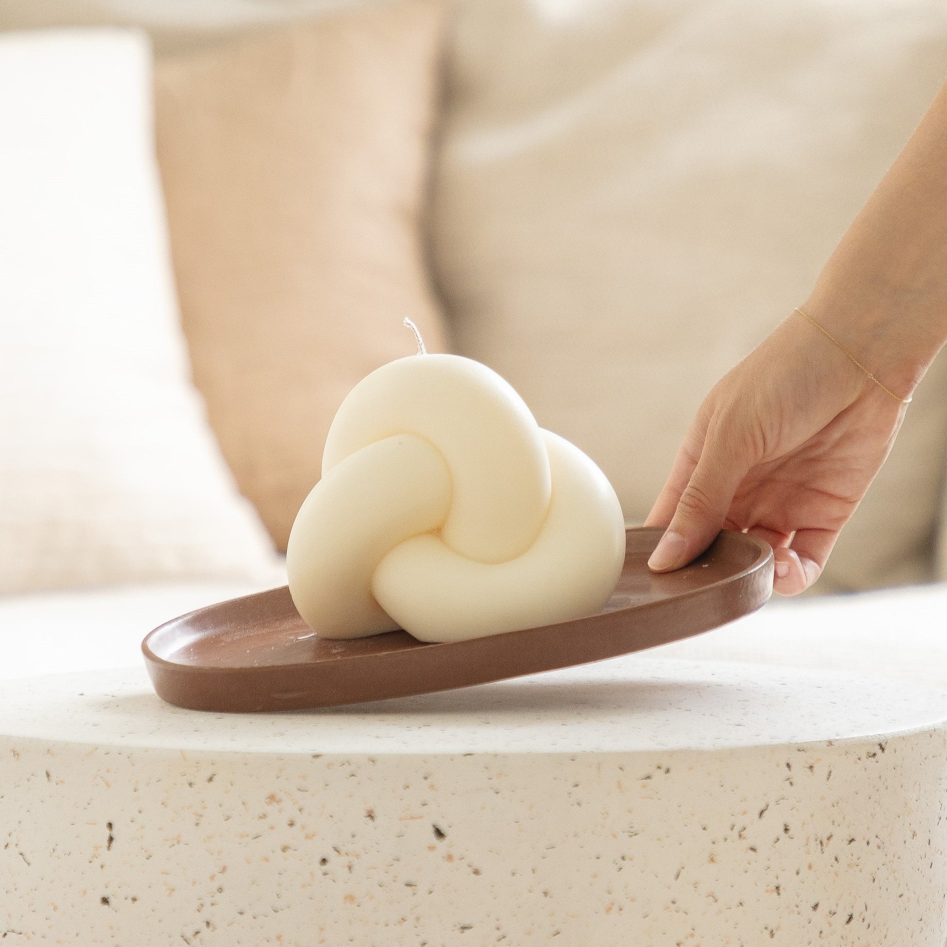 Hand holding a white cloud-shaped candle on a brown tray with a blurred background